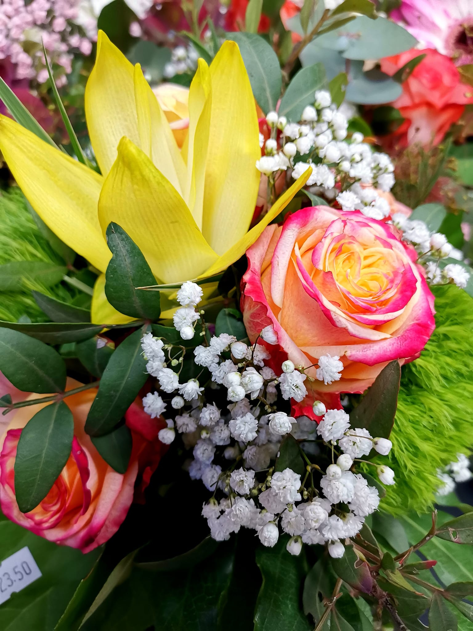 Nahaufnahme eines farbenfrohen Blumenstraußes mit gelben Lilien, zweifarbigen rosa-gelben Rosen und feinem weißen Schleierkraut.