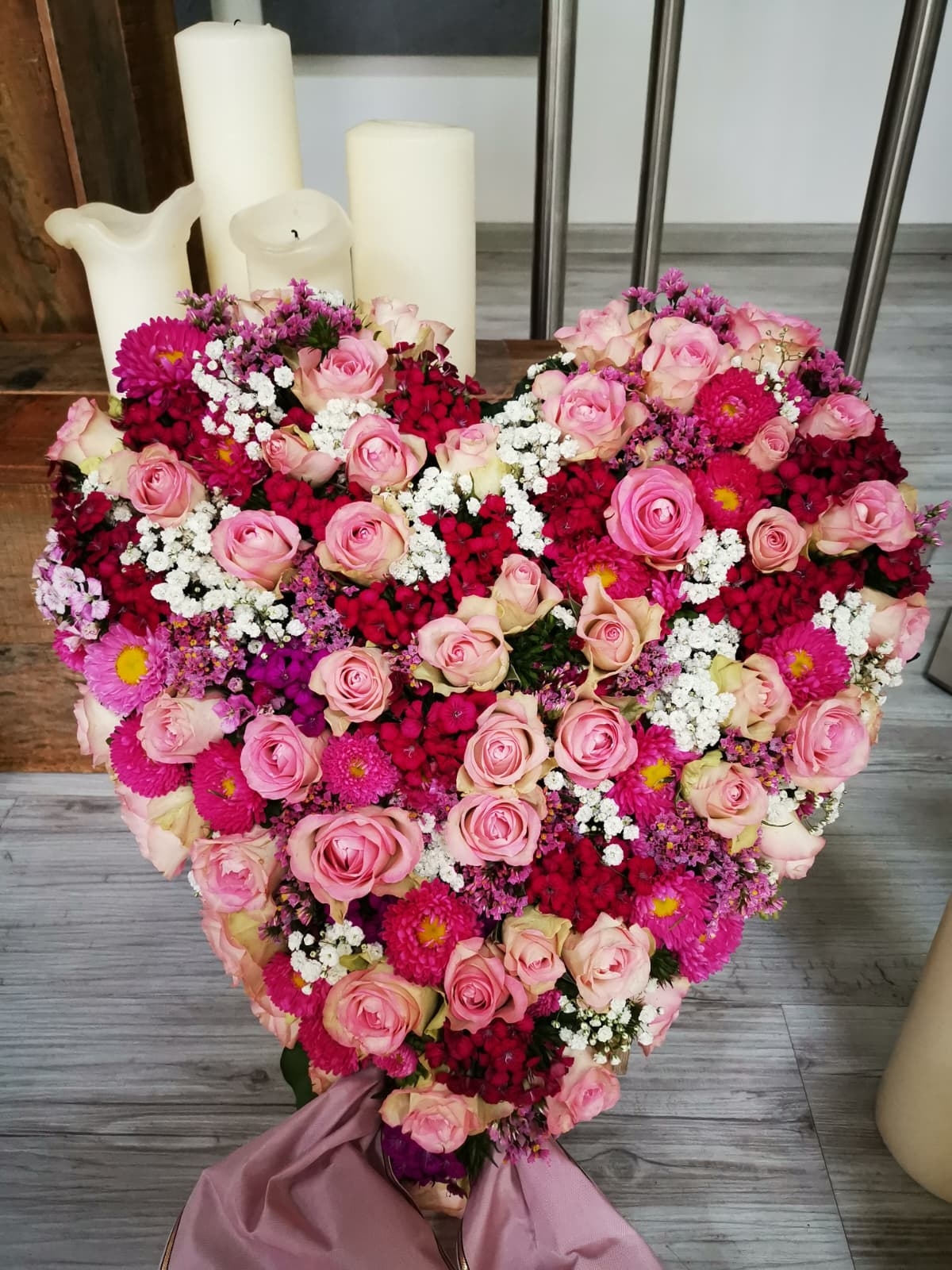 Herzförmiges Blumengesteck aus rosa und magentafarbenen Rosen, roten Nelken und Schleierkraut.