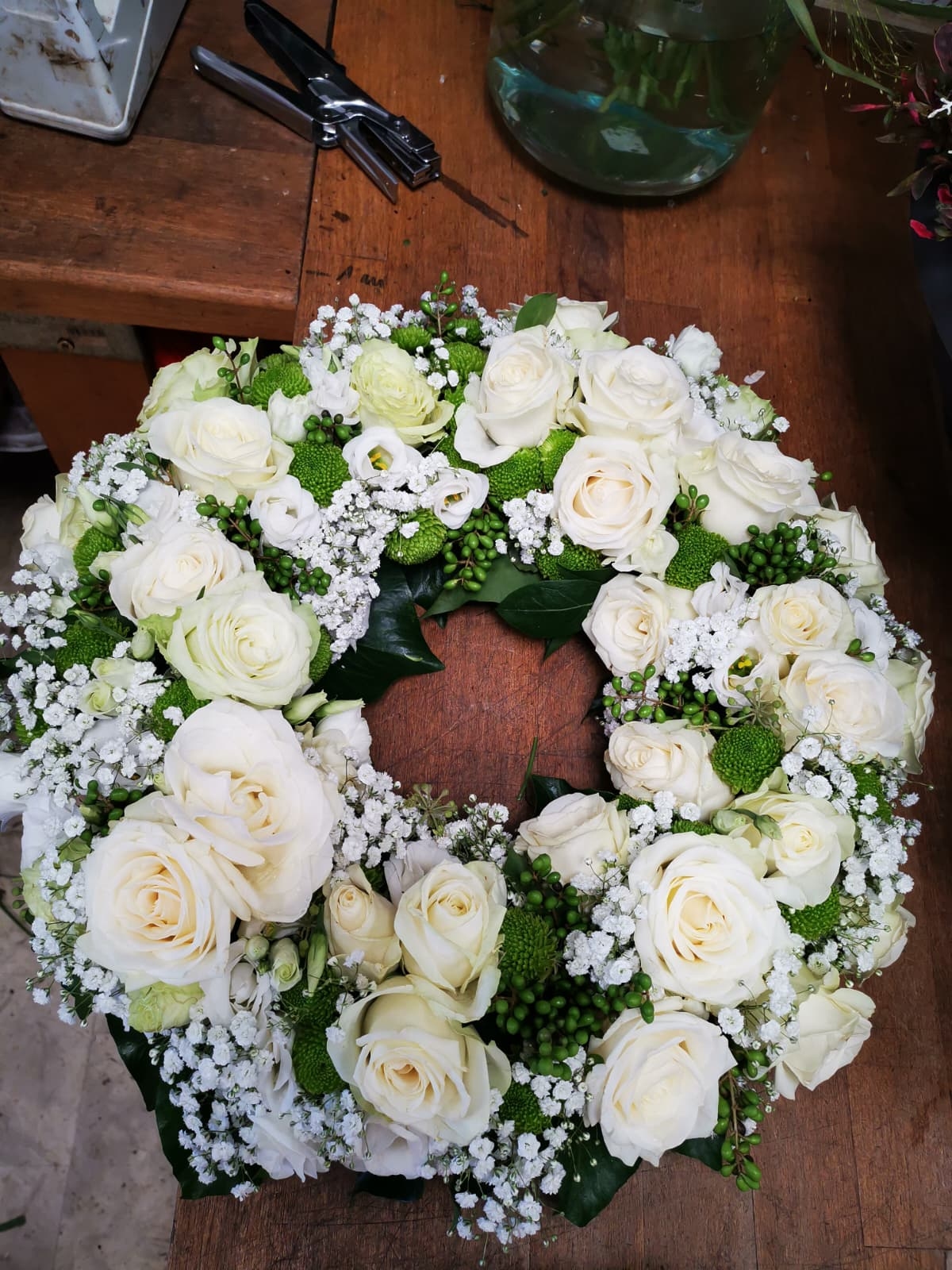 Trauerkranz aus weißen Rosen, Schleierkraut und grünen Beeren auf einer hölzernen Werkbank.